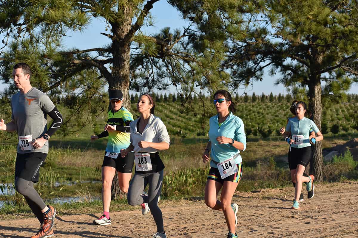 Six runners on an off-road trail around a lake surrounded by pine trees.