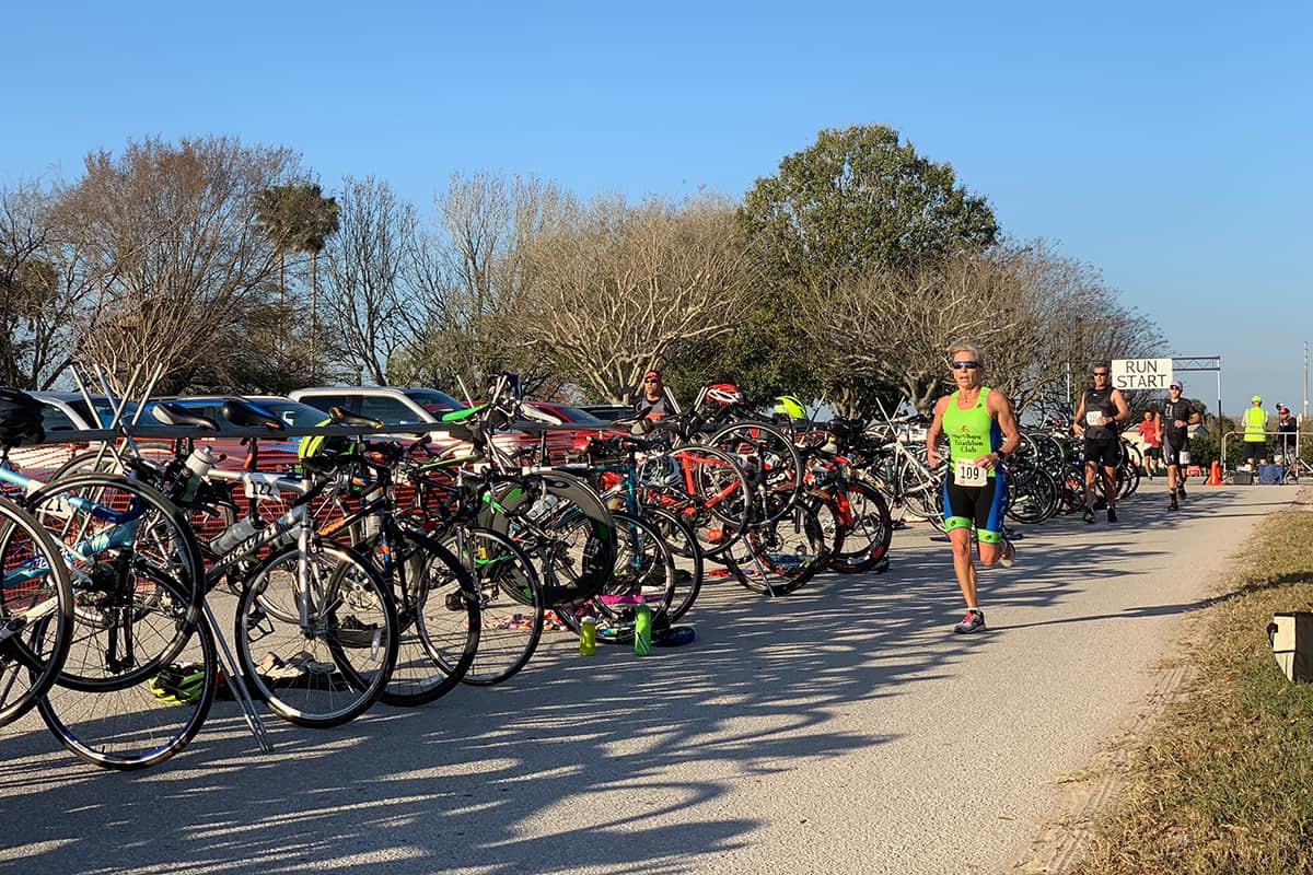 Runners run on a paved street alongside numerous parked bikes.