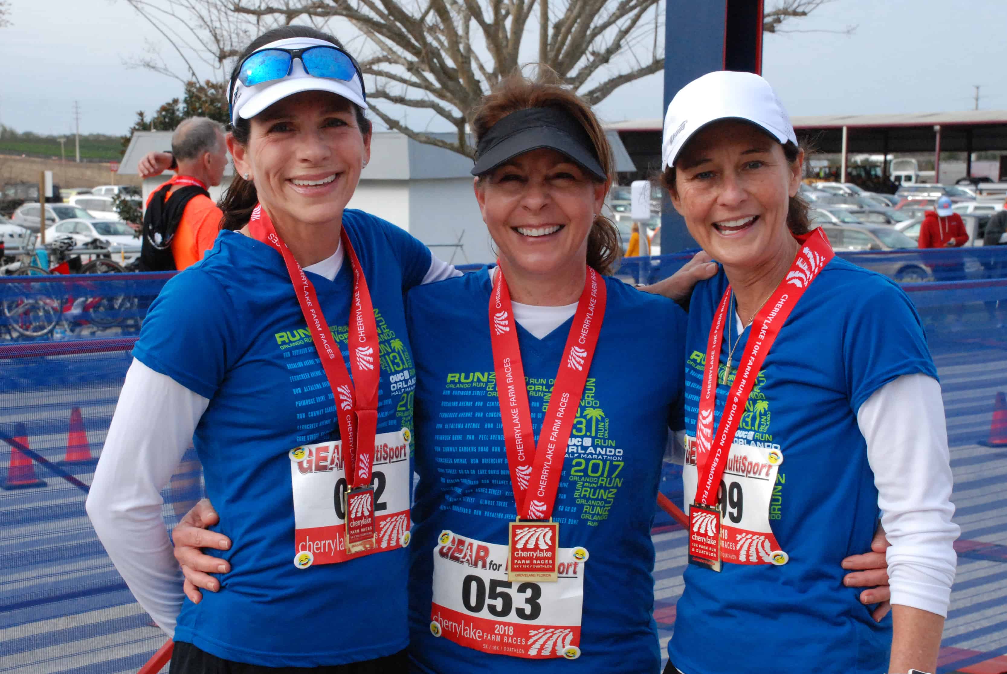 Three ladies wearing matching blue shirts stand together after a race at the finish line.