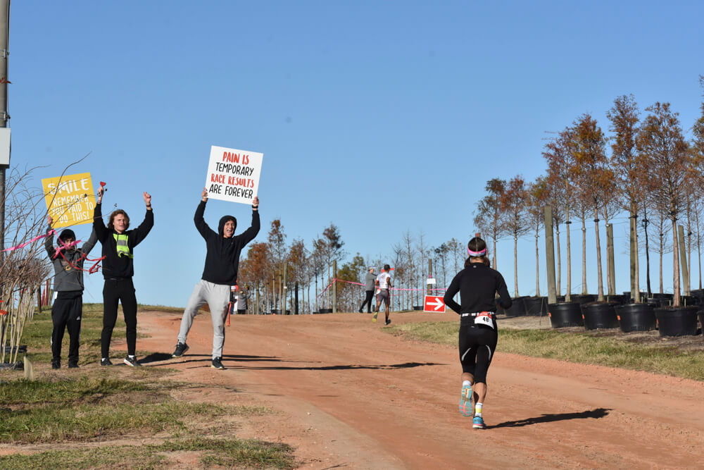 Three people holding signs, pumping their fists and shouting encourage a female runner.